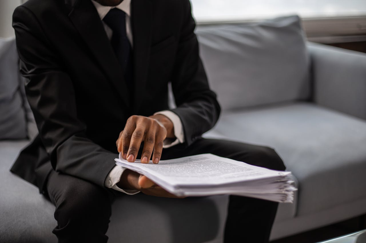 our-services-1 Close-up of a businessman in a suit reviewing documents while seated on a sofa indoors.