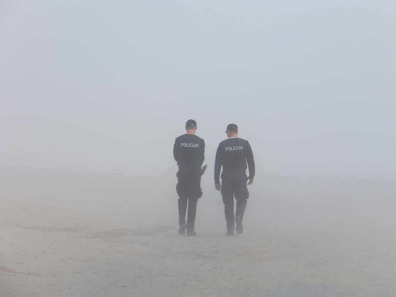 Two policemen walking on a foggy beach, creating an atmospheric scene.